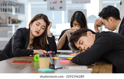 Asian young tired exhausted businesswoman in formal suit sitting napping on table while male female businesspeople colleagues closed eyes take break sleeping together after working late overtime. - Powered by Shutterstock