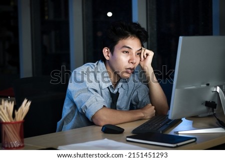 Asian young tired staff officer man using desktop computer having overwork project overnight in office, exhausted unhappy businessman feeling sleepy after after working hard overtime at night.