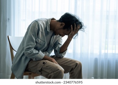 Asian young upset depressed man sitting alone in living room at home. Attractive unhappy male feeling very sad, lonely and frustrated with life problem think of money debt, budget loss, bankruptcy. - Shutterstock ID 2340776595