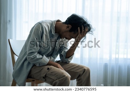 Asian young upset depressed man sitting alone in living room at home. Attractive unhappy male feeling very sad, lonely and frustrated with life problem think of money debt, budget loss, bankruptcy.