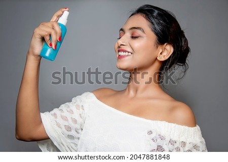 Asian Young woman with bottle spraying on her face. side face portrait isolated on gray background. skin care product.