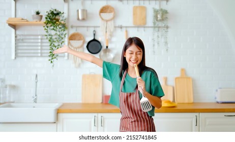 Asian young woman dancing in kitchen room. Female happy and relaxing at free time on weekend - Shutterstock ID 2152741845