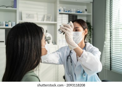 Asian Young Woman Doctor Using Flashlight On Patient's Eye In Hospital. Attractive Specialist Physician Wear Mask, Examining And Checking Eyesight For Lady In Clinic. Medical Insurance Service Concept