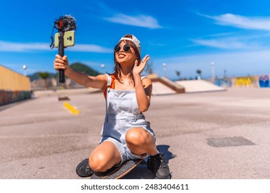 Asian young woman are doing livestreaming joyfully in skateboard urban park waving at the camera while recording - Powered by Shutterstock