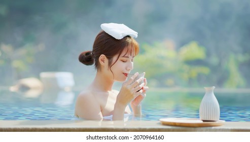 asian young woman is drinking sake while she relaxing sitting in hot spring with towel on head
