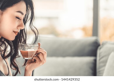 Asian Young Woman Drinks Coffee In The Morning While Sitting On Sofa Couch.