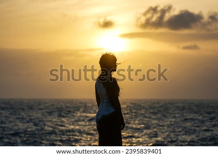 Asian Young woman enjoying freedom at the beach. Beautiful female model under sunset at seaside. Calm water reflects woman silhouette. Sun goes behind horizon. Girl is alone.