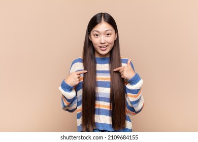 asian young woman feeling happy, surprised and proud, pointing to self with an excited, amazed look