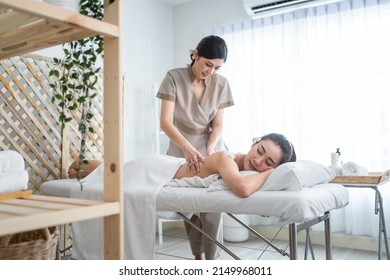 Asian young woman feeling happy and relax during back massage with oil. Attractive beautiful girl lying on massage table, getting physiotherapy from masseuse for skin and body care in spa beauty salon