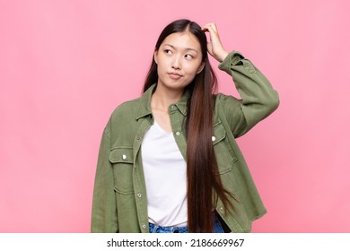 asian young woman feeling puzzled and confused, scratching head and looking to the side