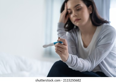 Asian young woman feeling shock after look at positive Pregnancy test. Disappointed attractive beautiful unplanned pregnancy girl sit on bed with upset and sad face for problem don't want to pregnant.