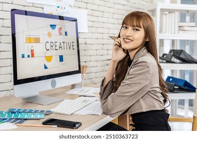 Asian young woman graphic designer smiling and looking at camera sitting at the desk with pc and tablet computer while working in office, Artist Creative Designer Illustrator Graphic Skill Concept - Powered by Shutterstock