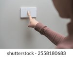 Asian young woman hand turn off on lighting switch at home room. Finger pushing light switch turn on or off white switch on wall for saving, control power electrical energy, eco environment concept.