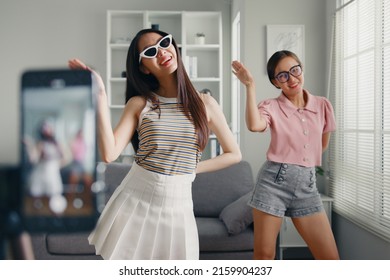 Asian young woman with her friend tiktoker created her dancing video by smartphone camera together. To share video on social media application