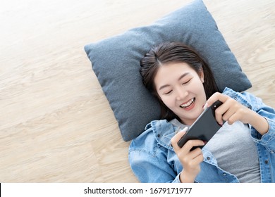 Asian Young Woman Lie Down On Wooden Floor Happiness And Enjoy Play Game Application From Mobile Phone Connect Internet With Copy Space