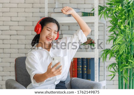 Asian young woman with long hair is listening to music from his smartphone with headphones on the sofa in the room. Stay at home in the outbreak situation of Covid-19