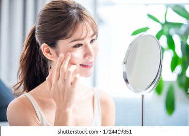 asian young woman look in mirror and apply moisturized cream or sunscreen on her face