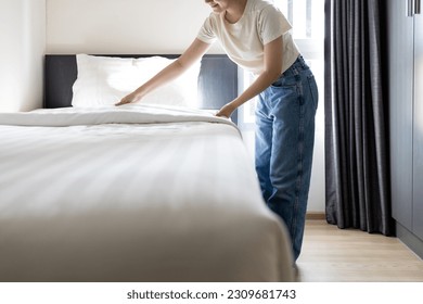 Asian young woman making bed arranging blanket,bedding in her bedroom after wake up,happy smiling teen girl cleaning the room,enjoy while doing housekeeping at home,housework,health hygiene  concept
