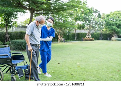Asian young woman nurse at nursing home take care and support disabled senior elderly man on walker or cane at backyard. Caregiver doctor and old patient wearing mask to prevent from Covid-19 pandemic