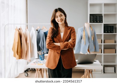  Asian young woman on desk in office of fashion designer and holds tablet, laptop and smartphone on desk - Powered by Shutterstock