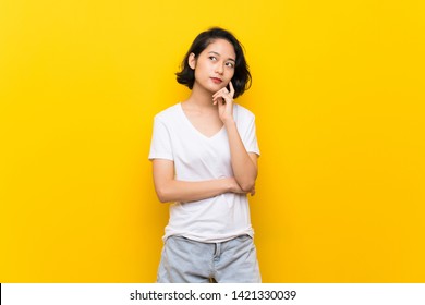 Asian Young Woman Over Isolated Yellow Wall Thinking An Idea While Looking Up