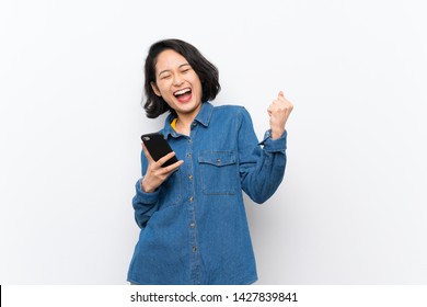 Asian Young Woman Over Isolated White Background With Phone In Victory Position