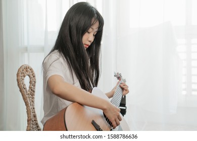 Asian Young Woman Playing Guitar In Bedroom