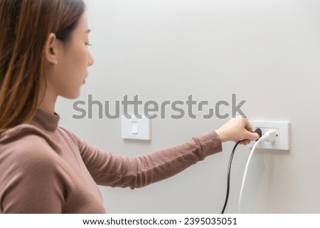 Asian young woman plugged in, unplugged electricity cord cable, put on or remove electric plug cable in socket on wall home outlet for saving, control power electrical energy, eco environment concept.