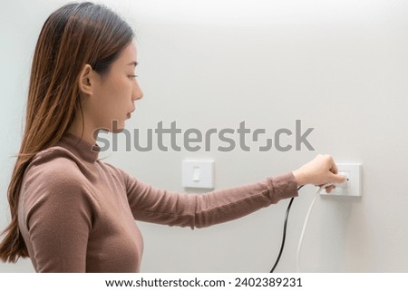 Asian young woman plugged in, unplugged electricity cord cable, put on or remove electric plug cable in socket on wall home outlet for saving, control power electrical energy, eco environment concept.