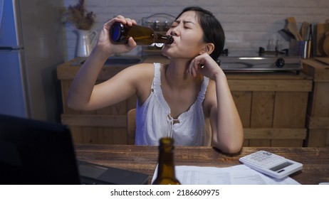 Asian Young Woman Propping On The Dining Table Drinking Beer Alone Is Looking Into Distance While Thinking About Her Financial Problems.