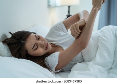 Asian young woman scratch hand feel suffer from allergy while sleeping. Beautiful attractive girl lying on bed in bedroom suffering from itching arm skin allergic reaction to insect bites, dermatitis.