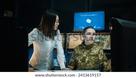 Asian young woman showing something to Caucasian female soldier and educating her on naval strategy in controlling army office. Educational marine military center for women concept.