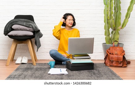 Asian Young Woman Sitting On The Floor Having Doubts And With Confuse Face Expression