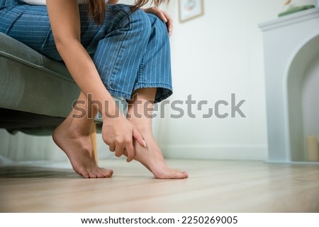 Asian young woman sitting on sofa holding her feet and stretch muscles have symptoms feeling pain, beautiful female problems with foot at home, painful ankle injury, Health care and medical concept