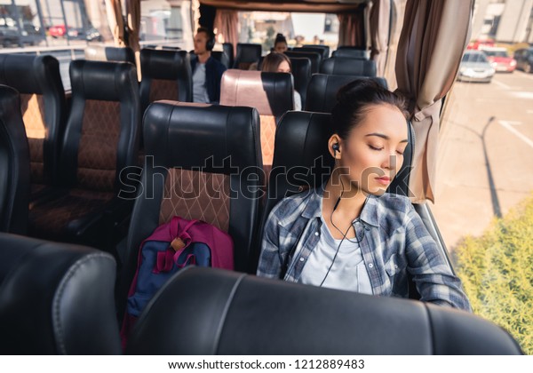 asian young woman sleeping and listening\
music in earphones during trip on travel bus\

