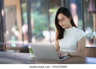 Asian young woman in smart casual wear working on laptop while sitting in creative office or cafe. young girl working with laptop on the wood table in the cafe