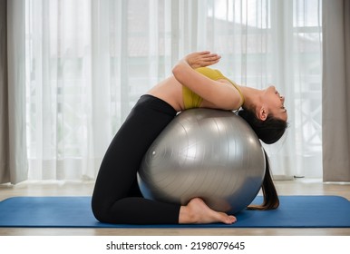 Asian young woman in sportswear doing abs exercises on a fitness ball for healthcare slim fit and body weight control at home. Female athletic practice yoga workout training by lotus position on ball.