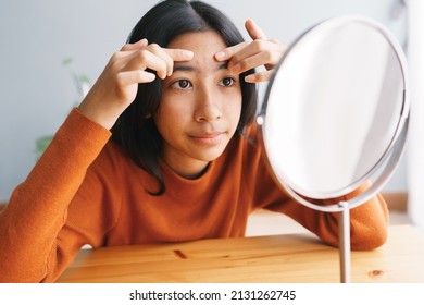 Asian young woman Squeezing acne skin and looking on the mirror at home, Close- up of young women face - Shutterstock ID 2131262745
