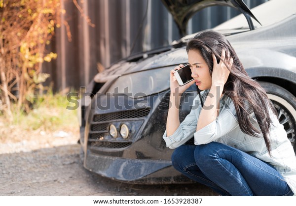 Asian young woman are stressed  and calling car\
insurance.Broken down car while traveling.Black long hair woman\
sitting and talking on cellphone after car breakdown trouble\
problem mechanic.