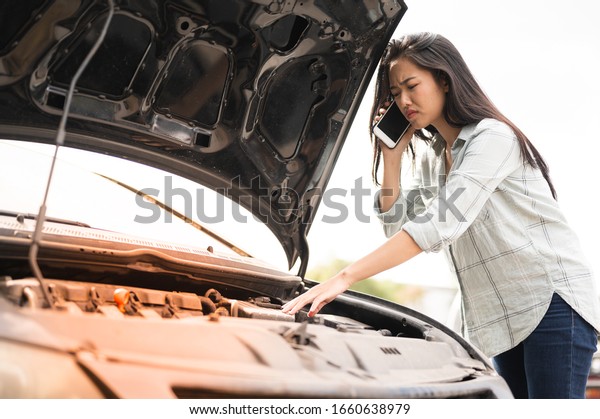 Asian young woman\
are stressed  and calling car insurance.Broken down car while\
traveling.Black long hair woman talking on cellphone after car\
breakdown trouble problem\
mechanic.