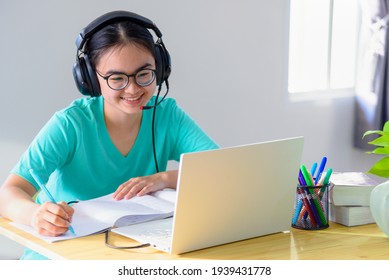 Asian young woman student with glasses headphones girl study happy writing note on a book looking video conference laptop computer university class online internet learning distance education at home - Powered by Shutterstock