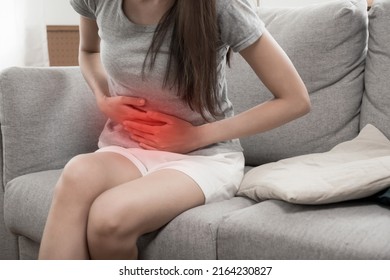 asian young woman suffering stomach ache sitting on couch in living room at home, people painful stomachache, gynecology, menstrual pain , medical and health care concept