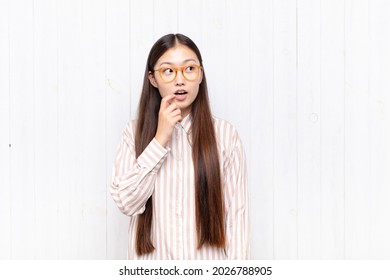 asian young woman with surprised, nervous, worried or frightened look, looking to the side towards copy space