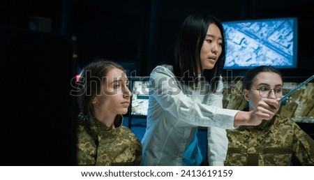 Asian young woman teacher demonstrating some documents and information to two Caucasian female soldiers and educating them in controlling army office. Educational military center for women.