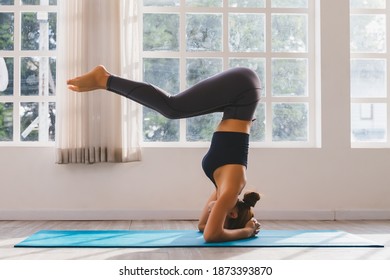 Asian young woman training yoga doing headstand pose on floor in room in morning. Instructor woman leading exercise pose, Healthy lifestyle, working out, indoor full length, studio background.