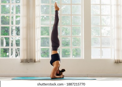 Asian young woman training yoga doing headstand pose on floor in room in morning. Instructor woman leading exercise pose, Healthy lifestyle, working out, indoor full length, studio background.