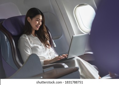 Asian Young Woman Using Laptop Sitting Near Windows At First Class On Airplane During Flight,Traveling And Business Concept