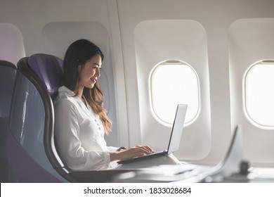 Asian Young Woman Using Laptop Sitting Near Windows At First Class On Airplane During Flight,Traveling And Business Concept