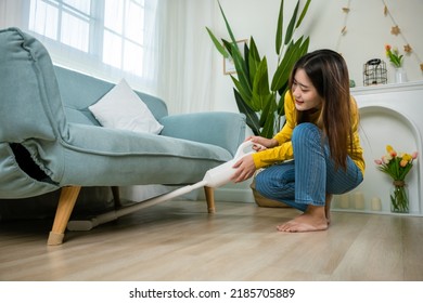 Asian young woman using vacuum cleaner dust while cleaning floor at home, homemaker easy cleaning with modern wireless vacuum cleaner near sofa in living room, housework concept