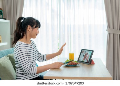 Asian Young Woman Virtual Happy Hour Meeting And Eating Food Online Together With Her Mother In Video Conference With Tablet For A Online Meeting In Video Call For Social Distancing.
